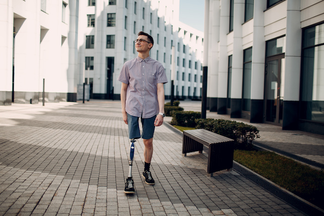 Disabled young man with foot prosthesis walks along the street.
